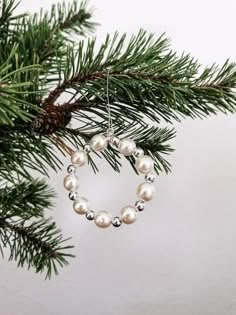 a christmas ornament hanging from a pine tree with white pearls and silver beads