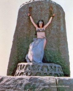 a woman in a blue dress laying on top of a large stone structure with her arms outstretched