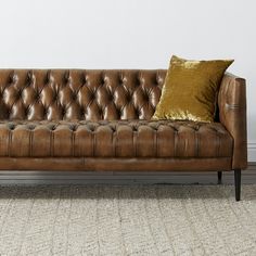 a brown leather couch sitting on top of a carpeted floor next to a white wall