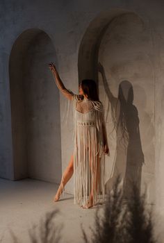 a woman standing in front of a wall wearing a white dress with fringes on it