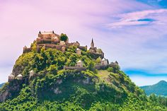 a castle on top of a mountain in the middle of water with trees around it