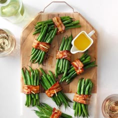 green beans and bacon wrapped in bacon on a cutting board next to glasses of wine