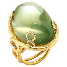 Synonymous with its name, a significant size of moonlit gemstone in everyday design serves as a timeless jeweled piece. Adularescence glows within this ring, an effect that resembles the appearance of a shimmering moon. The featured jewel is a mango moonstone with beautiful shades of green, mainly neutral sage, fashioned into an oval cabochon. When light strikes the surface of a gemstone, it exhibits a floating sheen like the moon. Depending on the angle, it also displays an attractive light and shades. The moonstone is set between four pieces of twisted 18k yellow gold woven into prongs. Underneath is a double shank that stretches like vines. The weight is 34.9 carats of moonstone. The ring measures 0.85 inches (width) by 1.06 inches (length) by 1.34 inches (height) by 0.59 inches (depth) The Angle, Moonstone Ring, Oval Cabochon, Shades Of Green, Fashion Rings, Moonstone, Vines, The Moon, The Ring