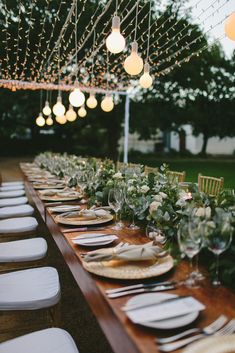 a long table set with plates and place settings for an outdoor dinner party in the evening