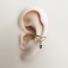 an ear is shown with a green stone in the middle and a gold chain hanging from it