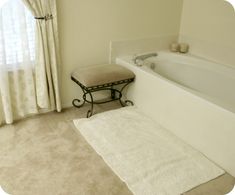 a white bath tub sitting next to a window in a bathroom on top of a carpeted floor