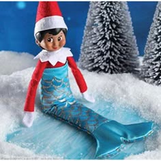 an elf is sitting in the snow next to some pine trees and wearing a blue dress