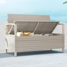 a white wicker storage bench with cushions on the ground next to a palm tree