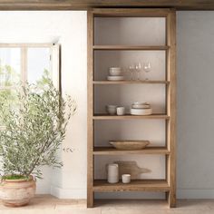 a wooden shelf with dishes on it next to a potted plant