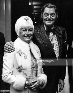 an older man and woman standing next to each other in front of a doorway with their arms around each other