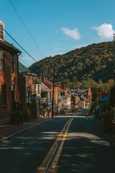 an empty street lined with brick buildings in front of a green mountain covered hill and blue sky