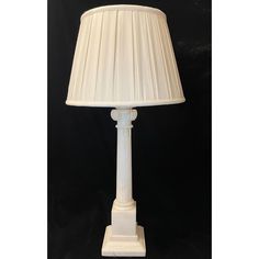 a white lamp on a black background with a light shade in the shape of a column