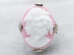 Sweet and full of detail, this Art Deco cameo ring is something special! The filigree is impressive, created using the die-stamping method that produces very fine detail while remaining strong and resilient. The pink glass cameo depicts a woman with 1920s styling, flowers set in curls, and an open neckline. Metal: 14K White Gold Gem: Glass Cameo Gem Measurements: 13.1 x 18.0 mm, Oval Ring Size: 3.25 SKU #: A36203 Each piece has been identified and graded by a Graduate Gemologist who has been cer Sterling Silver Cabochon Wedding Rings, Styling Flowers, Filigree Ring Gold, Art Deco Pink, Estate Ring, Estate Rings, Cameo Ring, Ring White Gold, Oval Ring