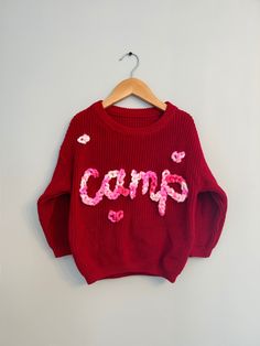 Valentines Custom Knit Sweater! The cutest hand embroidered sweater with a pink multicolor chunky yarn on an red sweater.  Sweaters are an oversized fit. Model is wearing 18-24 months sweater (but typically wears 18 month clothing). Stay true to size for baggy fit that will last even longer!  CARE: wash normal (recommended inside out but not necessary) and lay flat to dry to avoid yarn fuzzing.  For more info, questions, changes or customs- message us on here or on instagram @ campcoveco! Hand Embroidered Sweater, Valentines Sweater, Name Sweater, Valentines Outfit, Valentines Outfits, Embroidered Sweater, Red Sweater, Stay True, Chunky Yarn