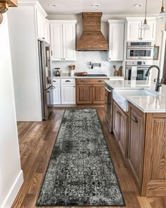 a kitchen with wooden floors and white cabinets, an area rug in the middle of the floor