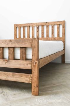 a wooden bed frame with no mattress on it in a white walled room next to a wood floor