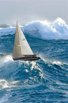 a sailboat in the middle of a large body of water with waves behind it