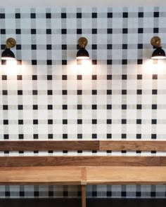 two wooden benches sitting next to each other in front of a wall with black and white tiles