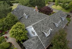 an aerial view of a house with many windows and roofing shingles, surrounded by lush green trees