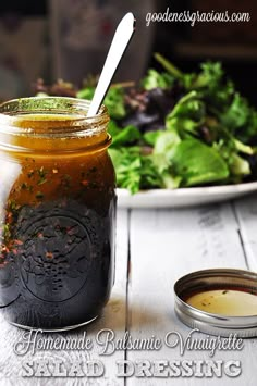 a jar filled with salad dressing next to a plate of salad greens and a spoon