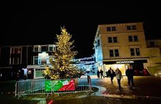 people are walking down the street in front of a lit up christmas tree at night