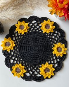 a crocheted doily with sunflowers on it next to some feathers