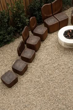 an outdoor fire pit surrounded by wooden chairs and graveled area with shrubbery in the background