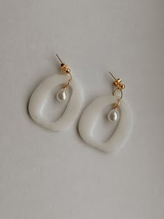 two pairs of white earrings with pearls hanging from the end of each earring, on a gray surface