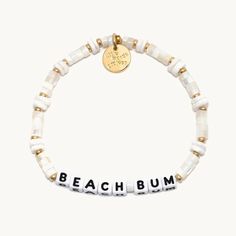 A white beaded bracelet that reads "beach bum. Cheap White Stretch Bracelet For Beach, Cheap Colorful Beaded Bracelets For Beach, Colorful Cheap Beaded Bracelets For Beach, Cheap Beachy Beaded Bracelets As Gifts, White Charm Bracelet For Beach, Cheap Summer Beach Pearl Bracelet, Beach Jewelry With White Letter Beads, White Beach Jewelry With Letter Beads, White Letter Beads Jewelry For Beach