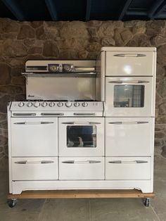 an old fashioned stove and oven are stacked on top of each other in front of a stone wall