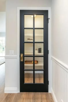 an empty room with a black door and white walls, hardwood flooring and hard wood floors