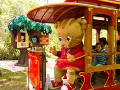 a large teddy bear riding on top of a red train car with people in it