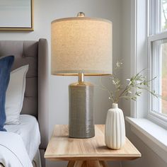 a table with a lamp and vase on it next to a bed in a bedroom