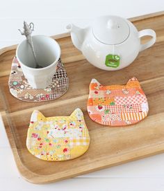 three pieces of fabric sitting on top of a wooden tray next to a tea pot