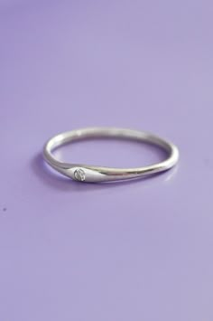 a white gold ring with a diamond on the side, sitting on a purple surface