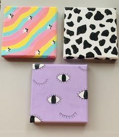 three painted canvases with different designs on them, one is purple and the other is pink