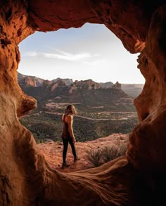 a woman standing in the middle of a cave looking out at mountains and desert land