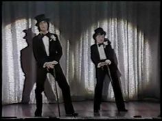 two men in tuxedos are standing on stage with canes and one is wearing a top hat