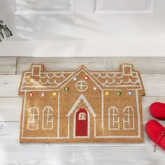 a door mat with a gingerbread house on it and red shoes next to it