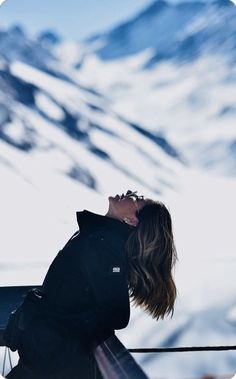 a woman standing on top of a snow covered ski slope next to a mountain range