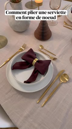 a white plate topped with a red bow tie next to gold forks and spoons