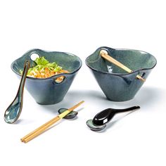 two bowls with chopsticks and salad in them on a white surface next to utensils