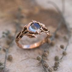 a gold ring with a blue stone in the center surrounded by flowers and leaves on top of a piece of wood