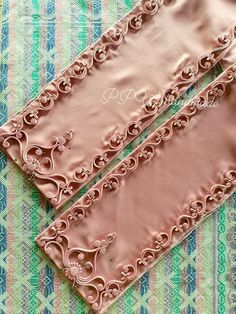 two pink satin gloves sitting on top of a green and blue patterned table cloth,