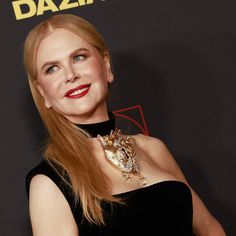 a woman with long red hair wearing a black dress and gold jewelry on her neck