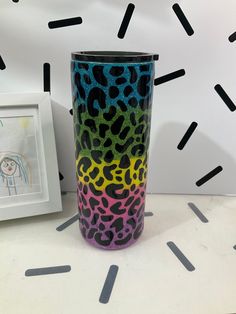 a colorful cup sitting on top of a white table next to a framed photo and black sprinkles