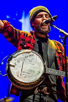 a man singing into a microphone and holding a large instrument in his right hand while standing on stage