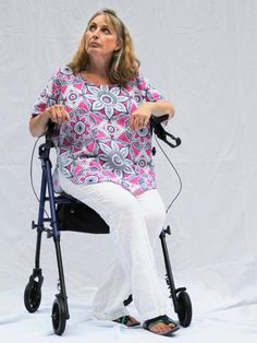 a woman sitting on top of a blue and white walker next to a white wall