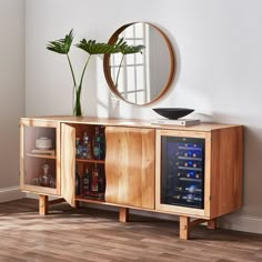 a wooden sideboard with a wine cooler in front of it and a round mirror on the wall