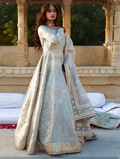 a woman in a white and gold gown standing on the ground with her hands behind her head